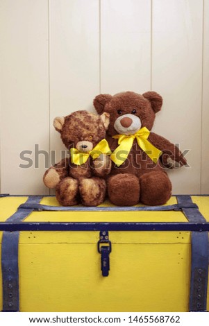 Two old bears sitting together on a yellow vintage chest.