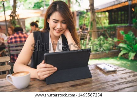Young attractive happy Asian business woman is using tablet or smartphone with smile face in coffee shop cafe, online shopping content, woman lifestyle background with copy space