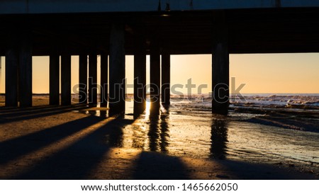 Sunrise at Galveston Island, Texas through pier on ocean and beach, shadows, water and sand Royalty-Free Stock Photo #1465662050