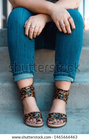 Female sitting down on the concrete steps. Hands crossed. Only legs and hands visible. Fashion concept. Silver rings, leopard shoes, jeans.