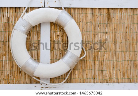 Single white   lifeboats that hang on a reed wall   at the seashore .