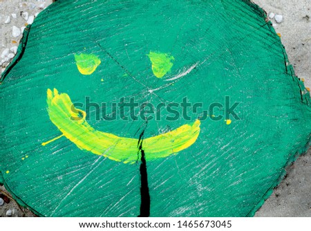 Close-up of green colorful tree trunk hand painted with a  yellow smiling face . 