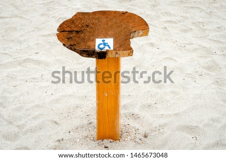 Wooden pole with painted sign which indicates that this  portion of beach is  for people with disabilities .
