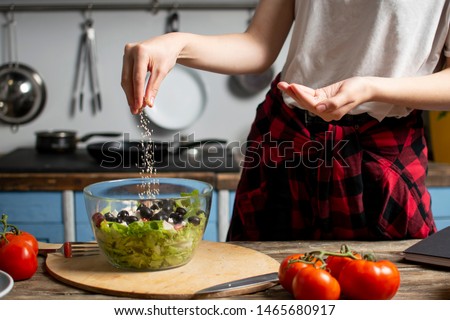 young cheerful girl prepares a vegetarian salad in the kitchen, she salts and adds spices, the process of preparing healthy food Royalty-Free Stock Photo #1465680917