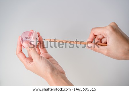 two hands using pink pig pencil sharpener to sharpen wooden pencil 