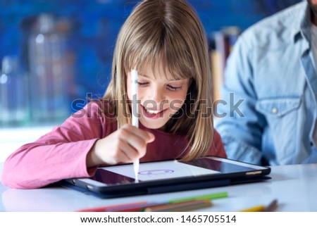 Shot of pretty happy little girl drawing with digital tablet at home.