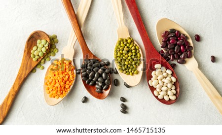 Different kinds of beans in spoons on white background