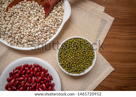The picture is a variety of whole grains, green beans, red beans, millet or job’s tears in a plate, placed on a brown tablecloth, wood grain, suitable for food advertising.
