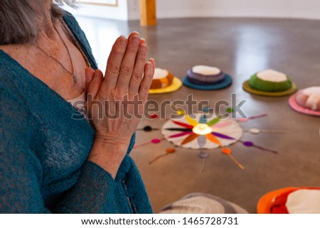Old woman prays in meditation room. Hands of a religious person are seen closeup, held together as she prays in a peaceful room, twelve colors of the Native American circle are seen in background.