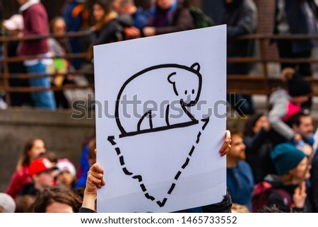 People protest against global warming. A close up view of a homemade poster held by an environmentalist, depicting a polar bear standing on a melting ice cap as people march in a city center.
