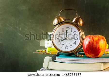 Stack of workbooks pens pencils alarm clock red apple on vintage scratched chalkboard background. Back to school education learning studying concept. Poster banner with copy space