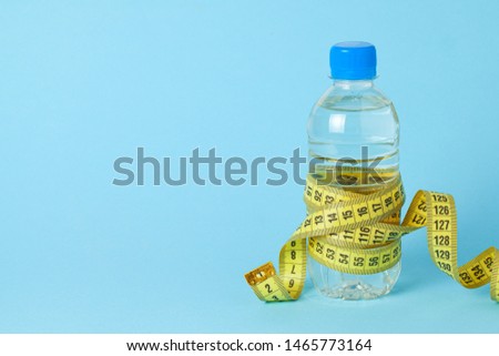 Plastic bottle with water and measuring tape on blue background. Copy space for text