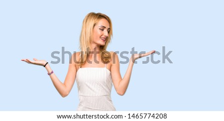 Young blonde woman holding copyspace with two hands over isolated blue background