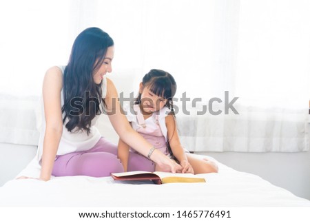 Happy mother and daughtermother reading a book to her daughterin bed together to enhance child development and learning to read relaxing in bedroom enjoy bedtime stories