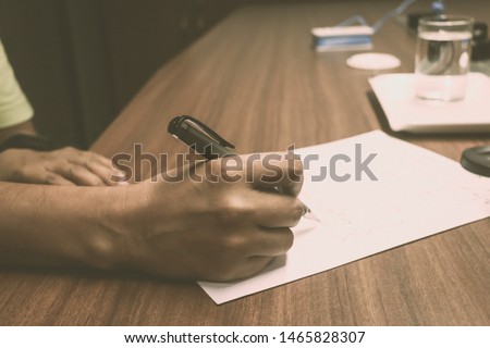 Side view shot of hands of a busy business man writing by pen in a sheet of paper at office desk. Businessman working on wooden table. Close-up. Vintage style. Copy space room for text.