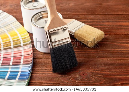 Two painting brushes, cans with paint, color guide palette on wooden table.