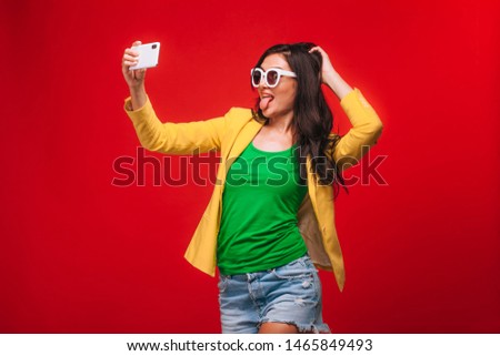 Girl on a red background in jacket takes a selfie on the phone
