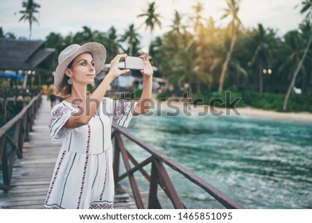 Vacation and technology. Outdoor portrait of pretty young woman taking photo with her smartphone on tropical beach.
