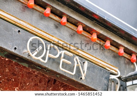 An old vintage neon OPEN sign lets customers know the business inside is operational when lit.