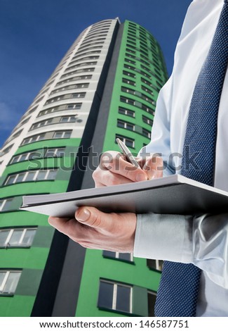 Businessman signing acceptance report / contract, modern highrise in the background
