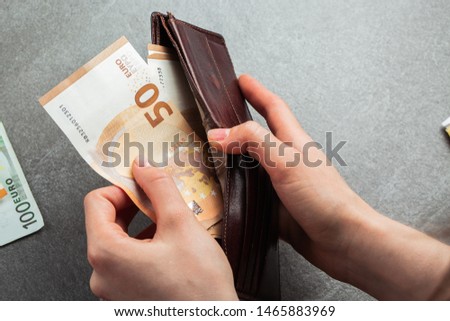 Girl is taking out a banknote of fifty euros from brown leather wallet. Hands, money and wallet close-up. charity. gray background. photo of money. payment. horizontal photo.