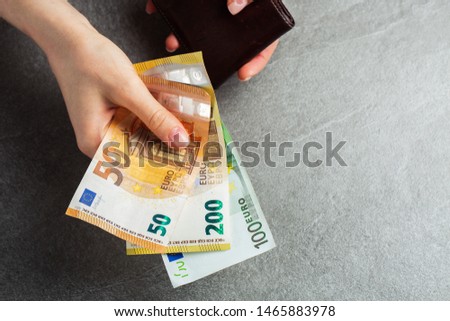 Girl is taking out a banknote of fifty euros from brown leather wallet. Hands, money and wallet close-up. charity. gray background. photo of money. payment. horizontal photo.
