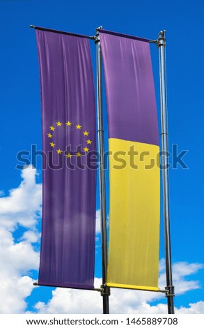 Vertical banners of Ukraine and the European Union on flag poles at blue sky with clouds. Two flags for your story about the political integration and economic cooperation between EU and Ukraine.