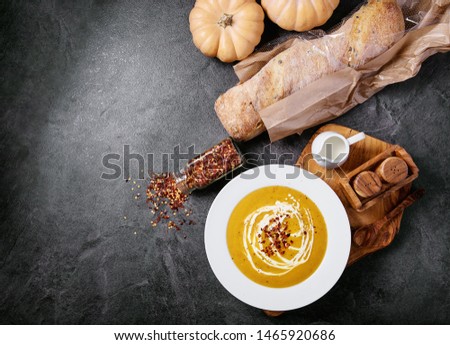 Pumpkin puree soup in white ceramic plate served with bread and pumpkins over dark texture background. Top view, flat lay