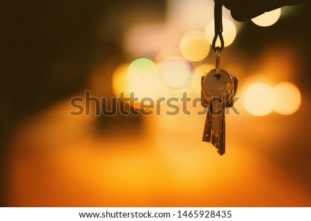 A set of modern metal keys hanging from above with a blurred background of yellow and orange lights. Keys on blurred bokeh background. Concept key photo