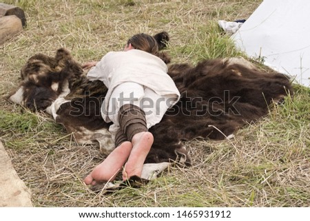 A young man in a folk shirt sleeps on a bear skin spread in the field in the summer.