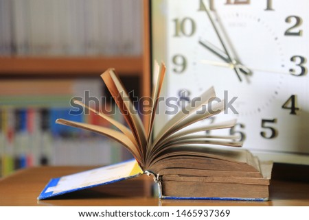 Close-up of old books open on the table in the library Wooden clock as background selective focus and shallow depth of field