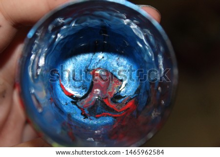 Hand holding cup with mixed metallic blue and red paint for pouring art technique against dark background Royalty-Free Stock Photo #1465962584