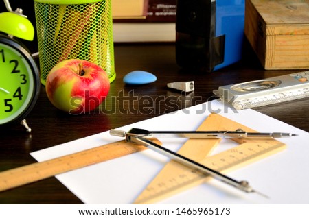 A4 sheet of paper, compasses, wooden square, wooden ruler, apple, pencil sharpener, eraser, wooden school pencil case on the desk.