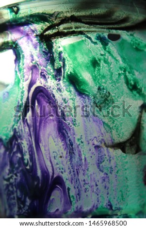 Cup with wet textured paint after acrylic paint pouring technique with shiny metallic colors. Aqua blue and purples. Colorful abstract background with high contrast and back lighting. Royalty-Free Stock Photo #1465968500