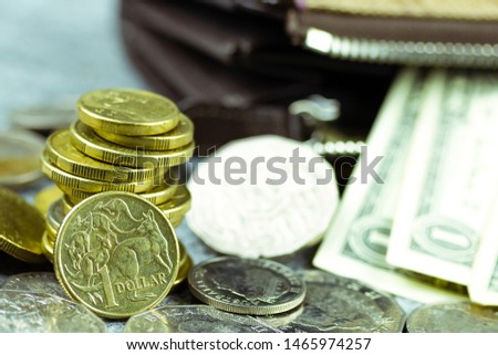 Australian dollar coins closeup with some one US dollar notes slipping out of the wallet in the background