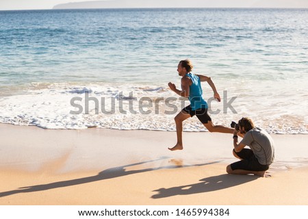 Behind the scenes of photo shoot of male sports athlete model running for photographer taking pictures for sport photoshoot. BTS on beach.