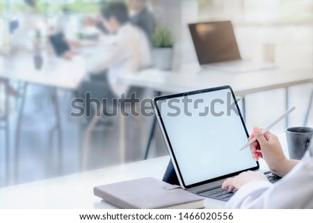 Cropped image of female hand using tablet with stylus pen while working in modern office with her team.