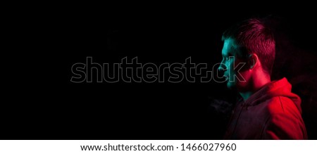 Close-up of the face of an unshaven face of a caucasian man looking away with stubble in the dark, illuminated on one side in Blue and on the other pink on a black isolated background. Cyberpunk style