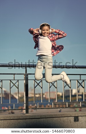 Like a rock star. Little girl jumping to music. Small happy child listening to music. Little child enjoying music playing in headphones. Cute music fan wearing wireless headset.