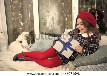 Opening christmas gift. Small cute girl received holiday gift. Best christmas gifts. Child excited about unpacking her gift. Kid little girl in beret hat hold box with bow at home window background.