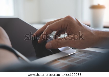 Interior designer, decorator, graphic designer finger touching on pro digital tablet screen while working with color swatch sample  on desk in studio office, close up.