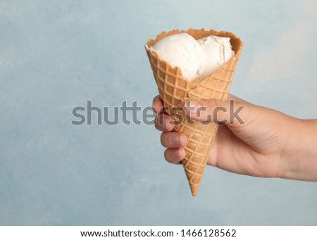Woman holding delicious ice cream in wafer cone on light blue background, closeup. Space for text