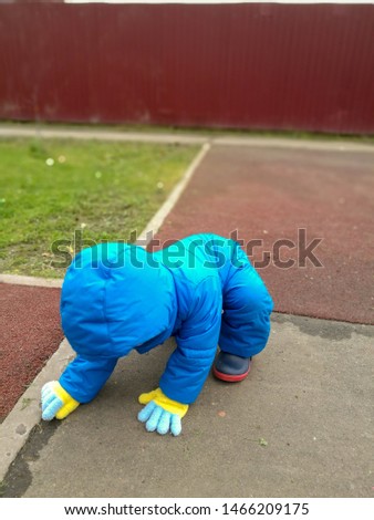 A little boy in blue autumn overalls and colored gloves examines something in a crack on the asphalt Royalty-Free Stock Photo #1466209175