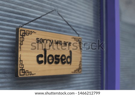Text "sorry we're closed" on wooden plate hanging on the metal shutter door