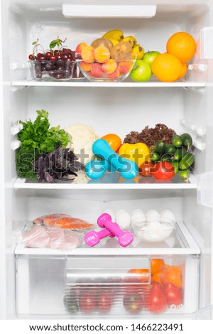 on the shelves of a white refrigerator, a stock of fresh vegetables, fruits, berries, fish, meat, eggs, cottage cheese, as well as pink and blue dumbbells for sports