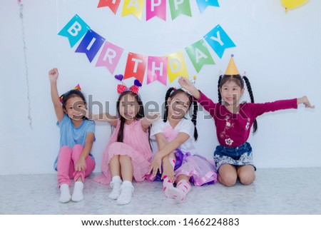 Concept Children's Party : Group of four cute little girls sitting together, smiling brightly at a party celebration and raising their hands with fun.
