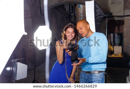 adult photographer and model discussing picture on camera display during photo session on city street