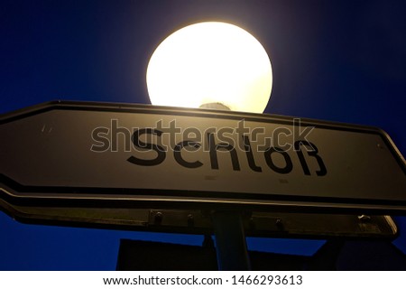 Signpost to the castle (German: Schloß) under a street lamp in the night