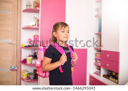 Little cute caucasian smiling pupil in school uniform preparing to school lessons with pink backpack at home. Childhood, school, education concept