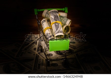 Small shopping cart with rolled up one hundred dollar banknotes on wooden background
